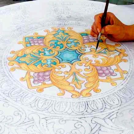 Una mano dipinge a colori un decoro ceramico floreale